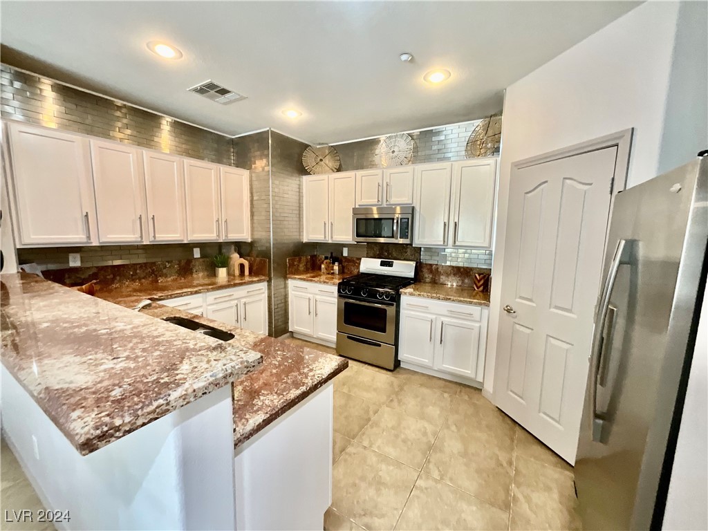 Kitchen with white cabinets, brown stone counters, stainless steel appliances, and a large foreground peninsula.
