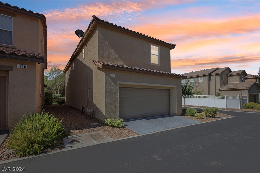 Two-story stucco home with an attached garage and desert landscaping beneath a pink dusk sky.