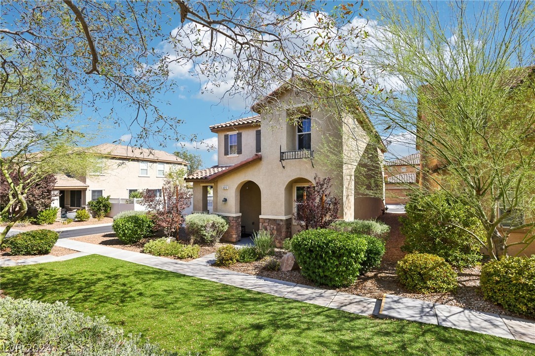 Two-story stucco home with arched entry, stone accents, balcony, and landscaped front yard.