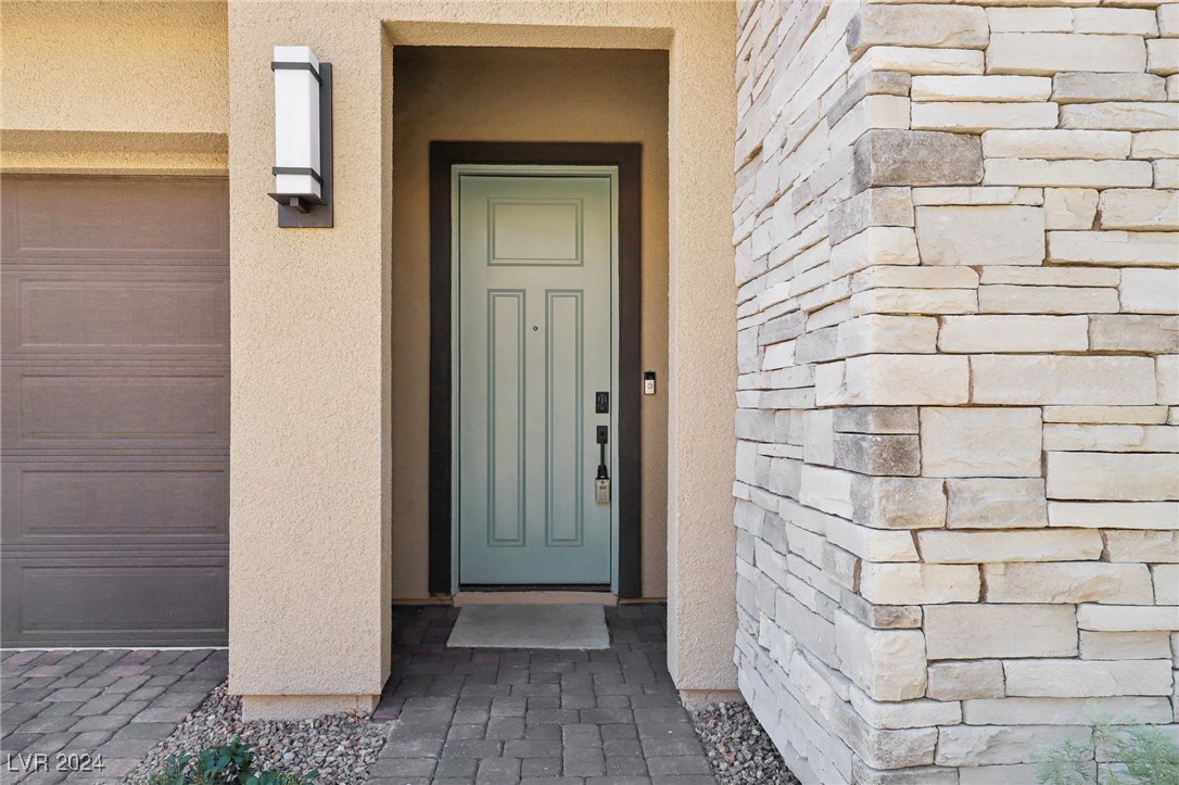 Home entrance with a pale green front door, stacked-stone wall, and paved walkway.