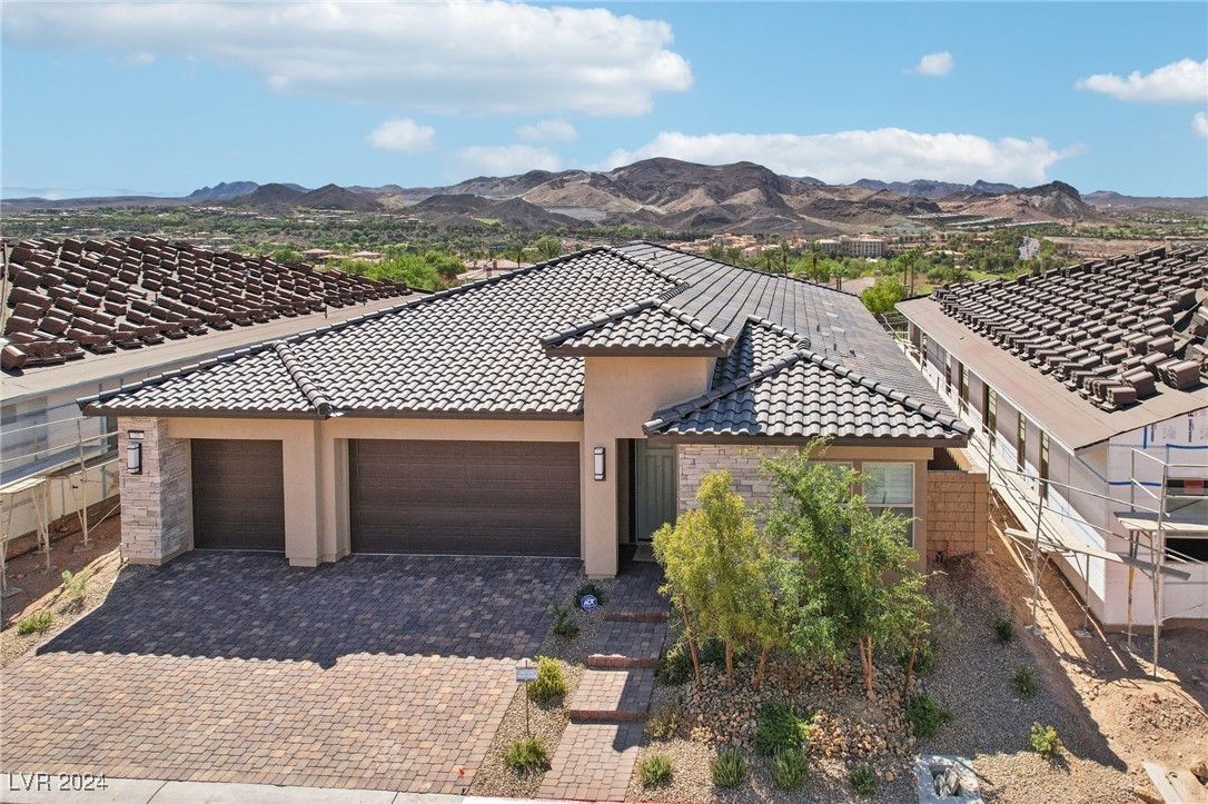 Single-story stucco home with a tiled roof and paver driveway, backed by distant mountains.