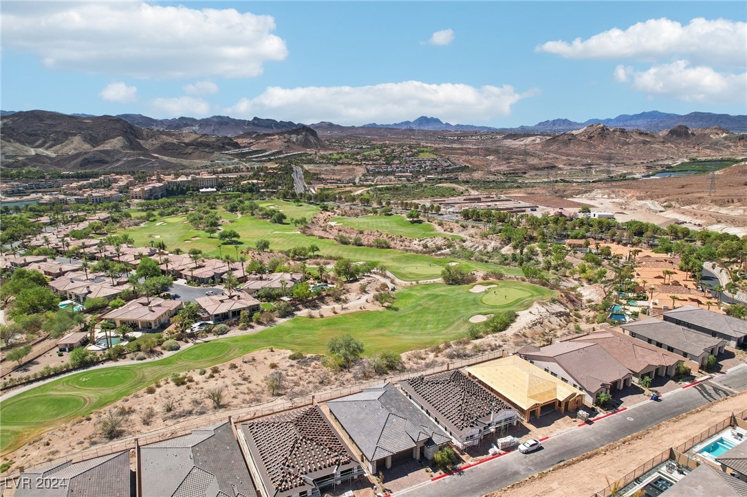 Aerial view of a golf course community with desert mountains and homes under construction.