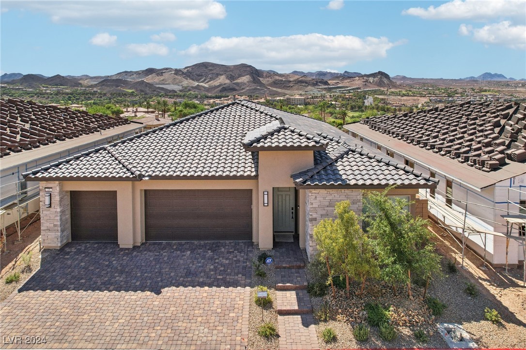 Single-story stucco home with a tiled roof, stone accents, and desert mountains behind it.