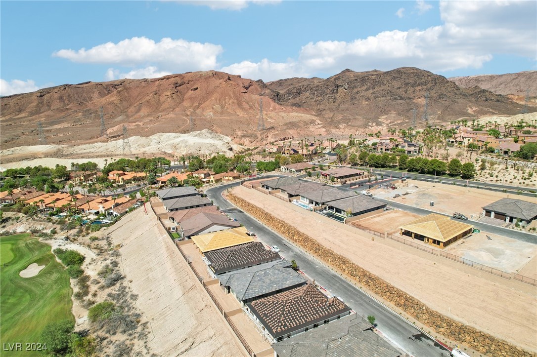Aerial view of homes under construction beside a golf course, with desert mountains beyond.