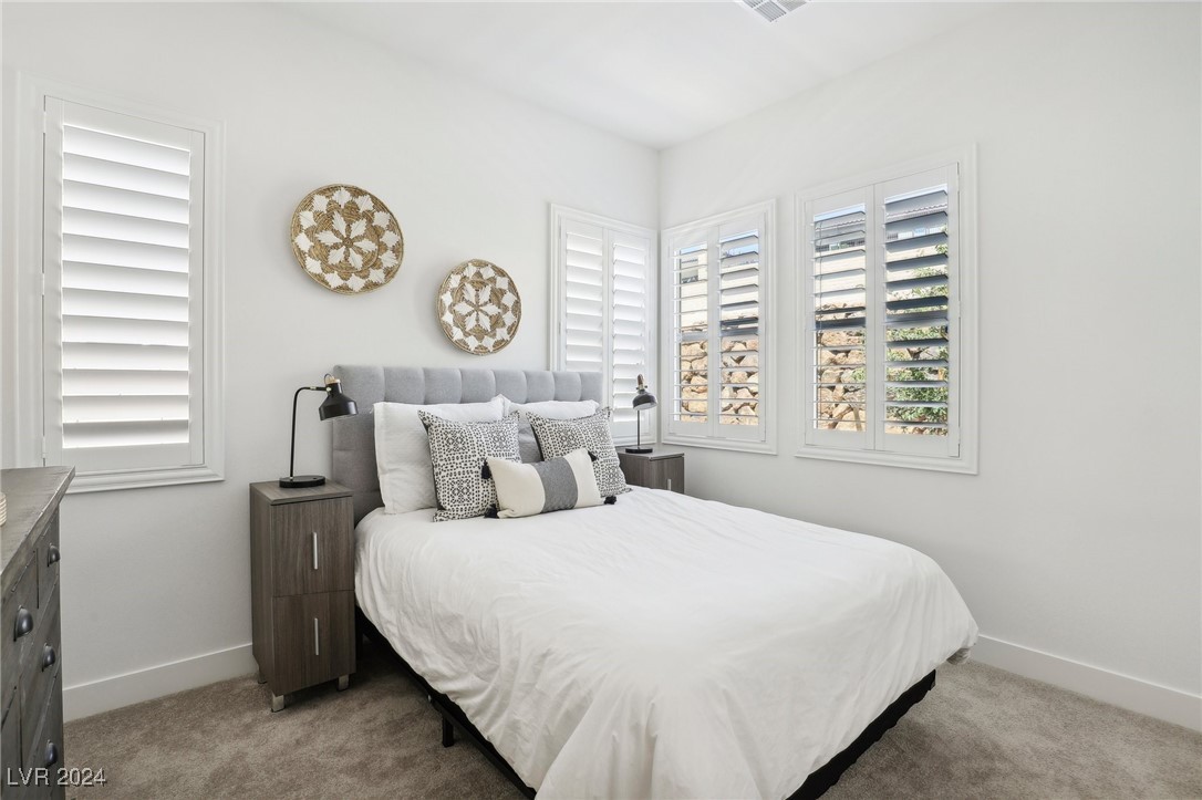 Bedroom with a white bed, gray headboard, patterned pillows, and plantation shutters.