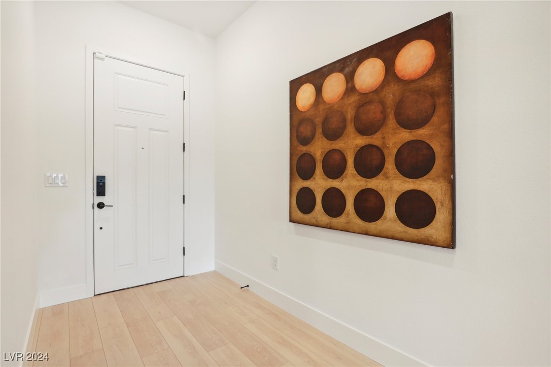 Entryway with a white front door, light wood flooring, and large circular wall art.