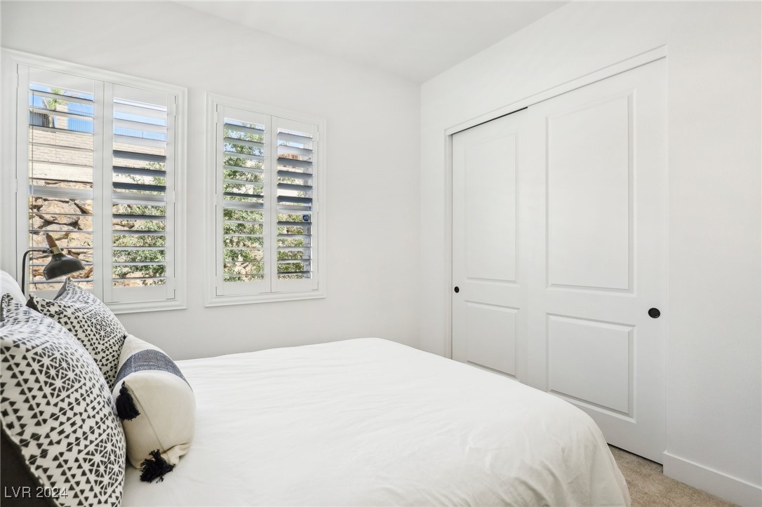 Bright bedroom with a white bed, patterned pillows, plantation shutters, and sliding closet doors.