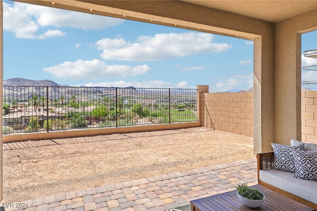 Covered patio overlooking a golf course and distant mountains, with cushioned seating and a paver border.