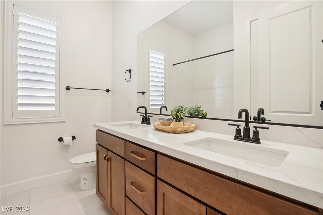 Bathroom with a long wood vanity, white countertop, large mirror, and plantation shutters.
