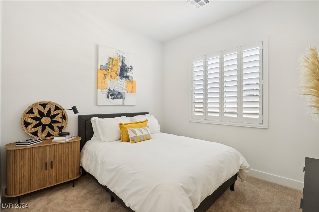 Bedroom with a white bed, yellow accent pillows, wood nightstand, and plantation shutters.