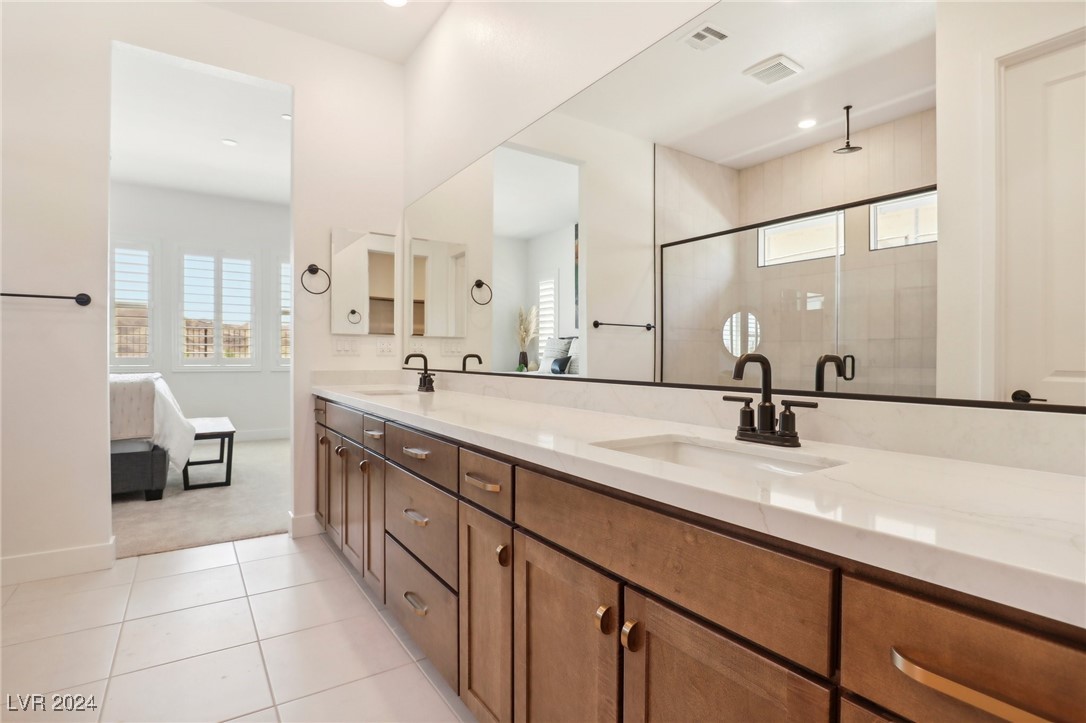 Bathroom with a long double vanity, warm wood cabinets, and a mirrored view of the tiled shower.
