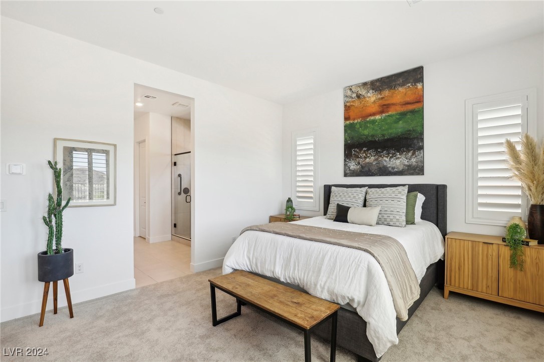 Staged bedroom with a king-size bed, colorful abstract painting, shuttered windows, and a bathroom doorway.