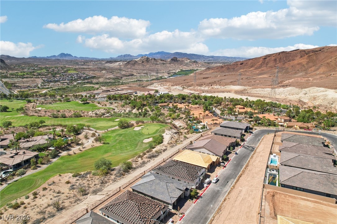 Aerial view of homes beside a golf course, with desert hills and mountains beyond.