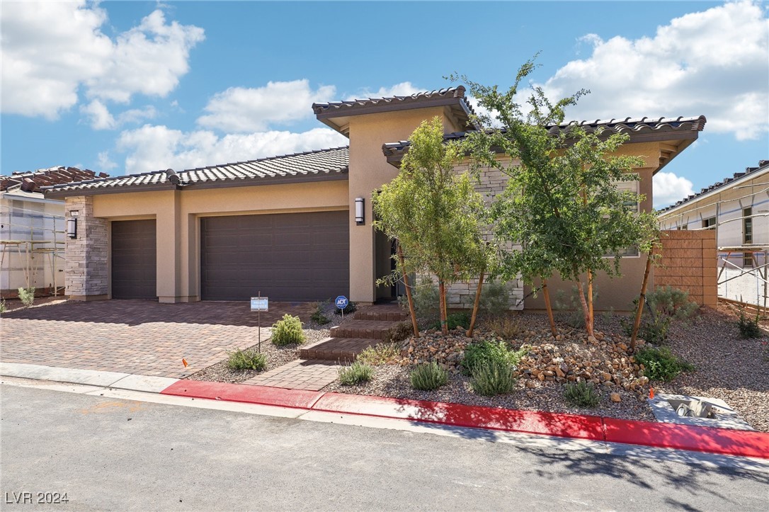 Tan stucco and stone home with a two-car garage, paver driveway, and desert landscaping.
