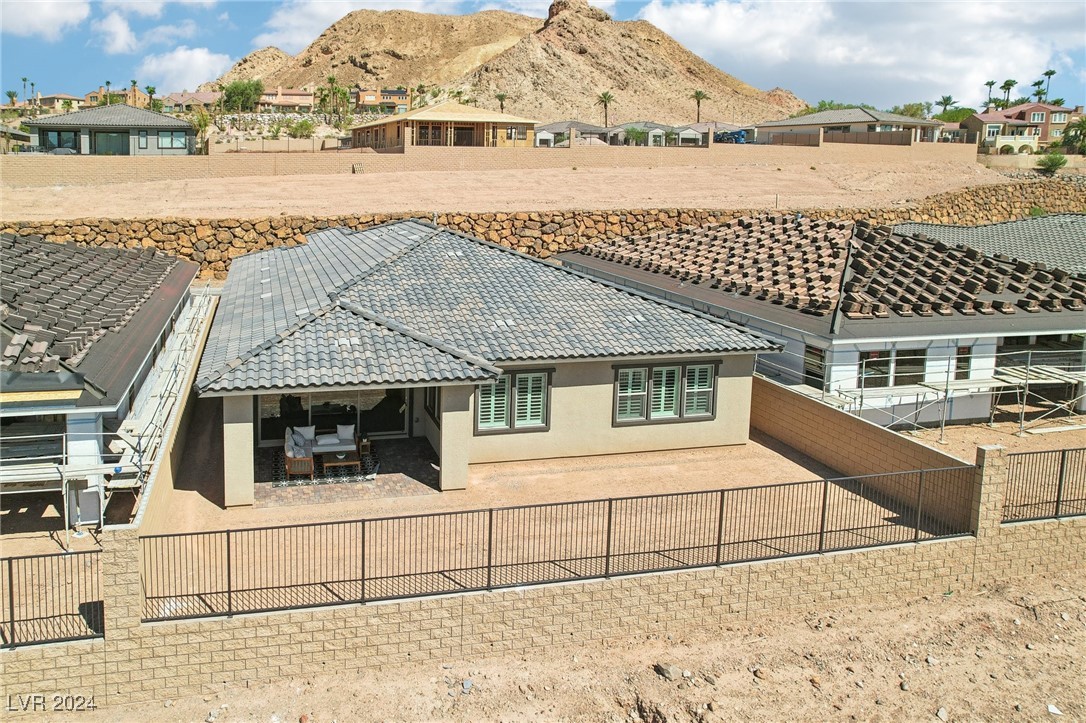 Single-story home with a covered patio and fenced yard below a rocky mountain backdrop.