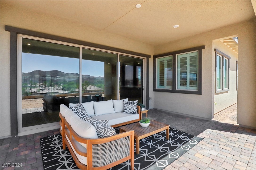 Covered patio with a white-cushioned sectional and coffee table, overlooking mountains through sliding glass doors.