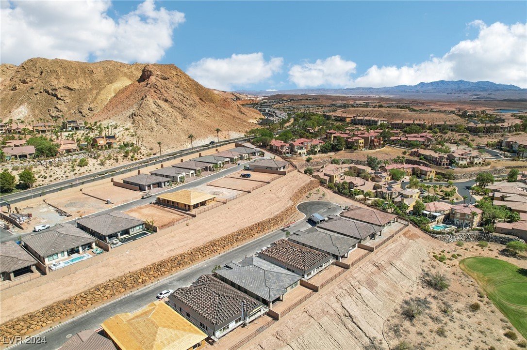 Aerial view of homes and graded lots beside rocky desert mountains and a golf course.
