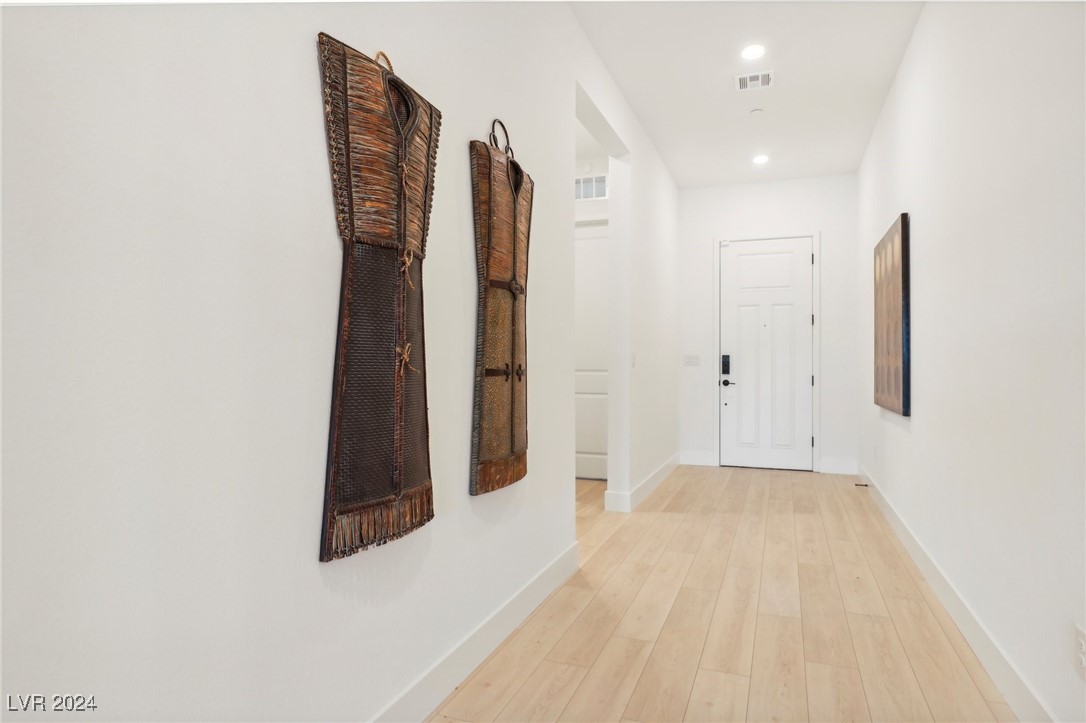 Entry hallway with pale wood flooring, a white front door, and tall woven wall decorations.