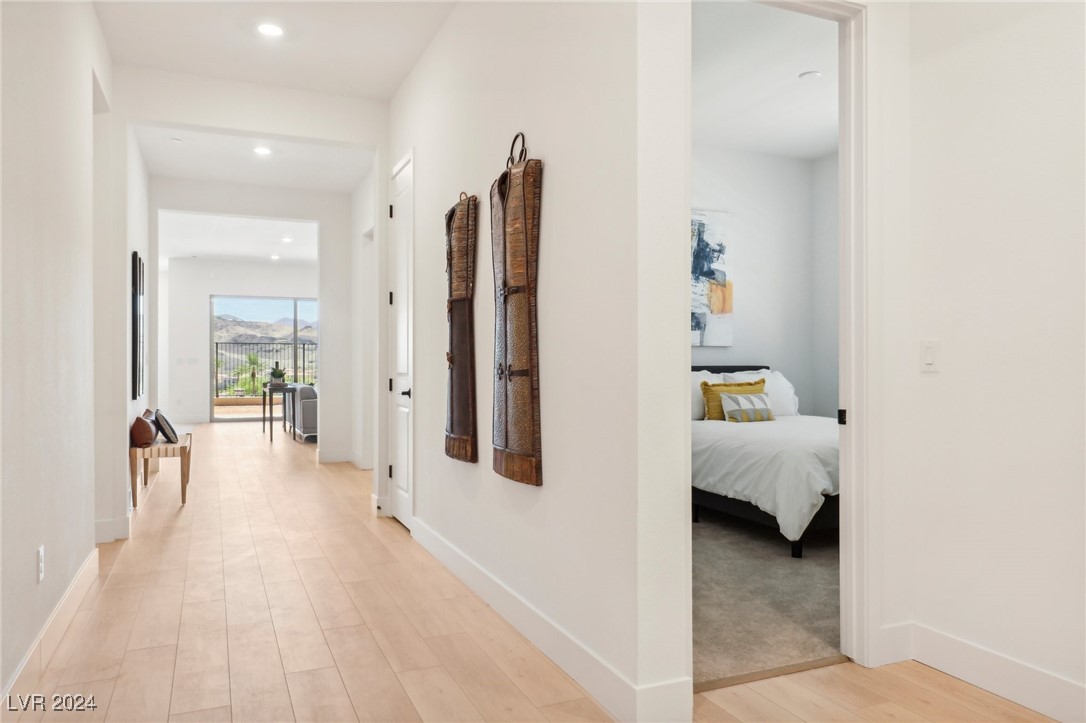 Bright hallway with pale wood floors, a bedroom doorway, and distant mountain views through glass doors.