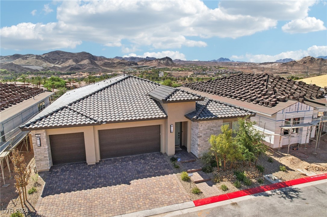 Modern single-story home with a three-car garage, surrounded by new construction and backed by desert mountains.