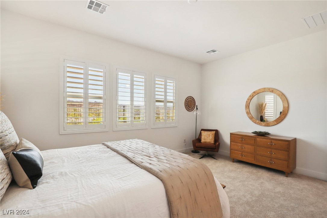 Bright bedroom with plantation-shuttered windows, a large bed, and a wooden dresser with a round mirror.