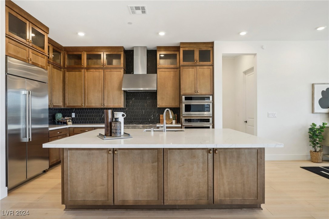 Kitchen with a large quartz island, wood cabinetry, black tile backsplash, and stainless steel appliances.