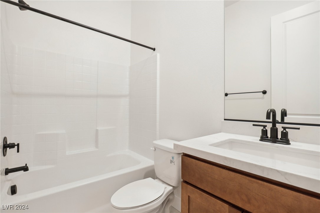 Bathroom with white tub-shower, tiled niche, toilet, and wood vanity.
