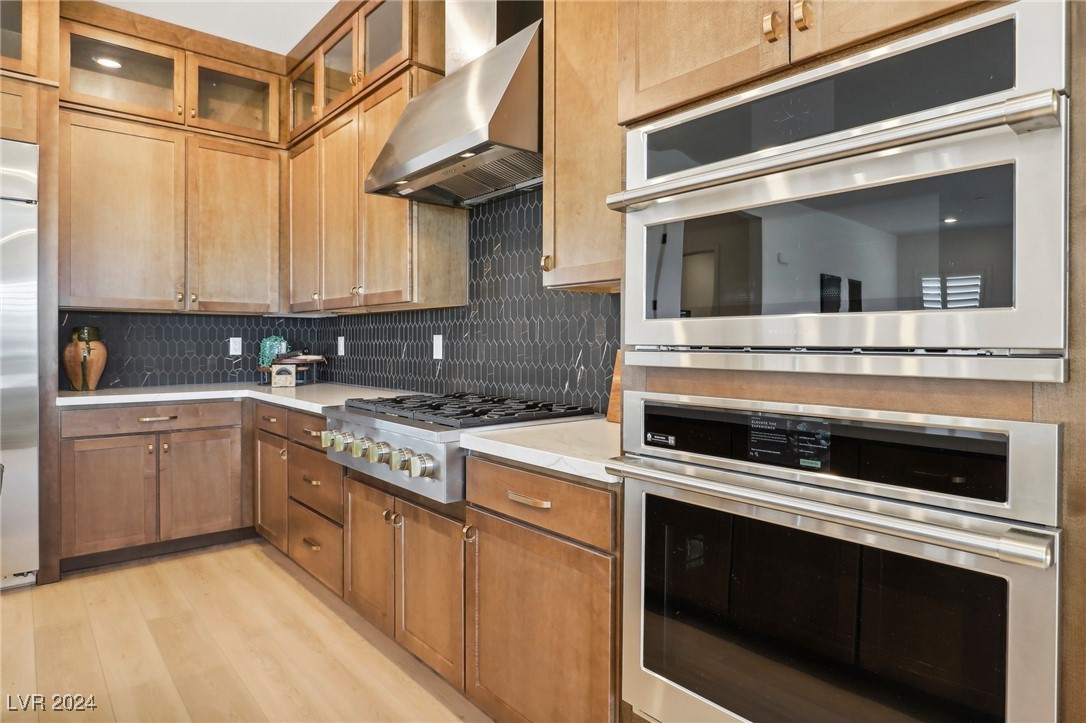 Kitchen with warm wood cabinets, dark hexagonal tile backsplash, gas cooktop, and built-in stainless steel appliances.