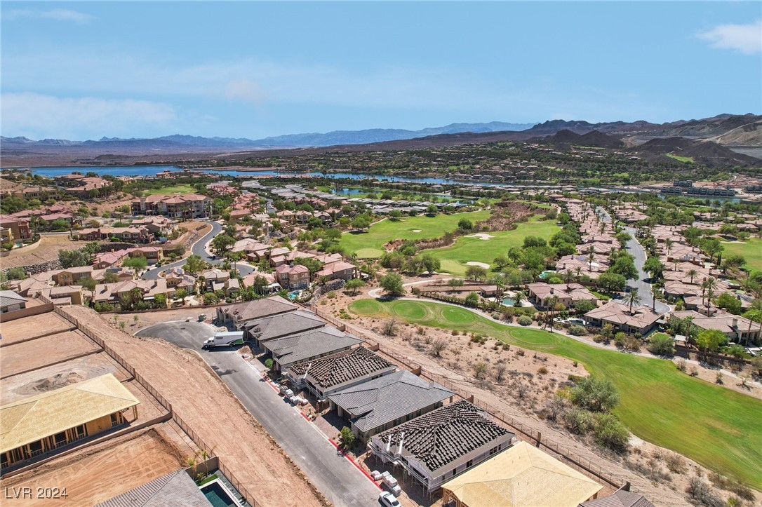 Aerial view of homes around a golf course, with a lake and mountains beyond.