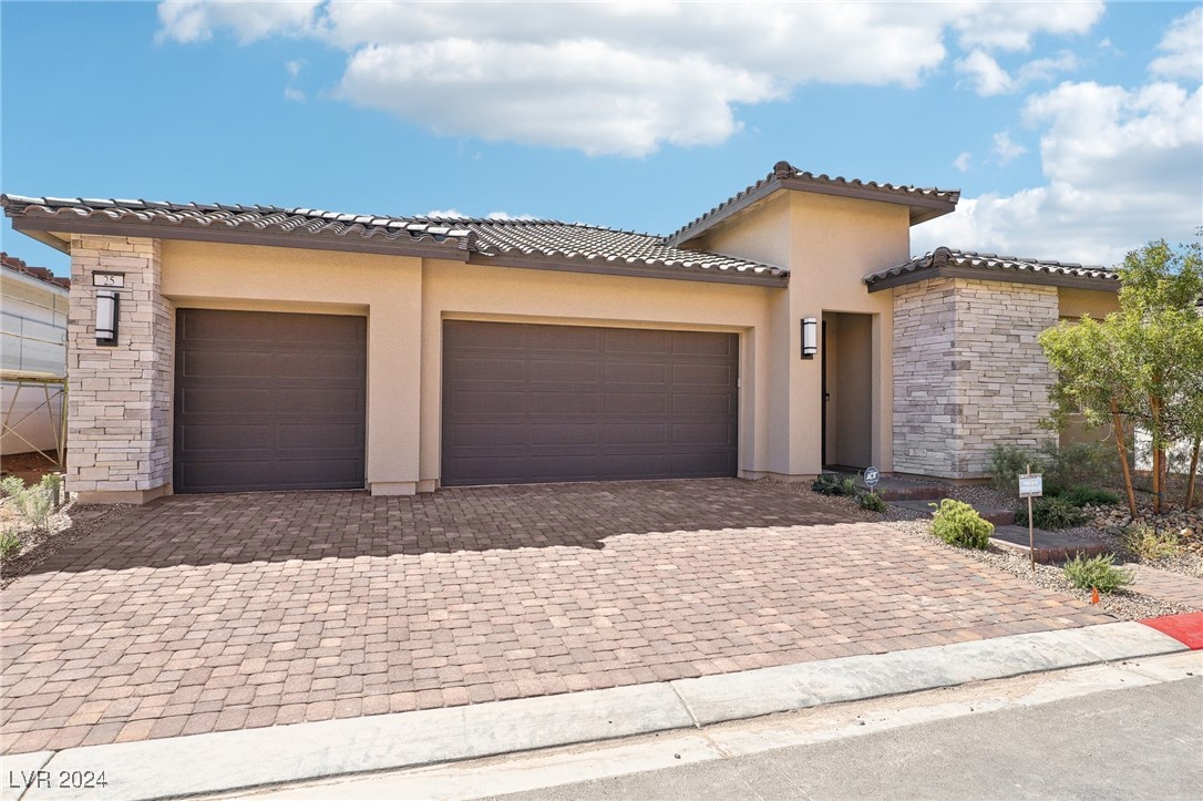 Home exterior with two dark garage doors, stone accents, and a wide paver driveway.