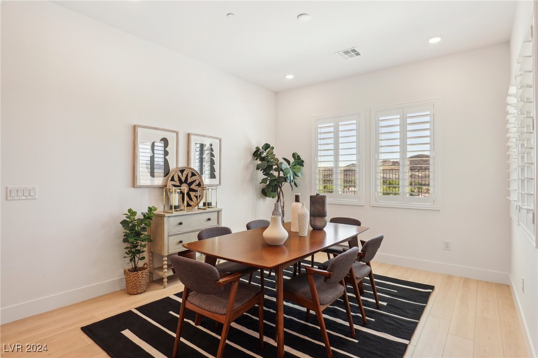 Dining room with a wood table, upholstered chairs, striped rug, and plantation shutters.