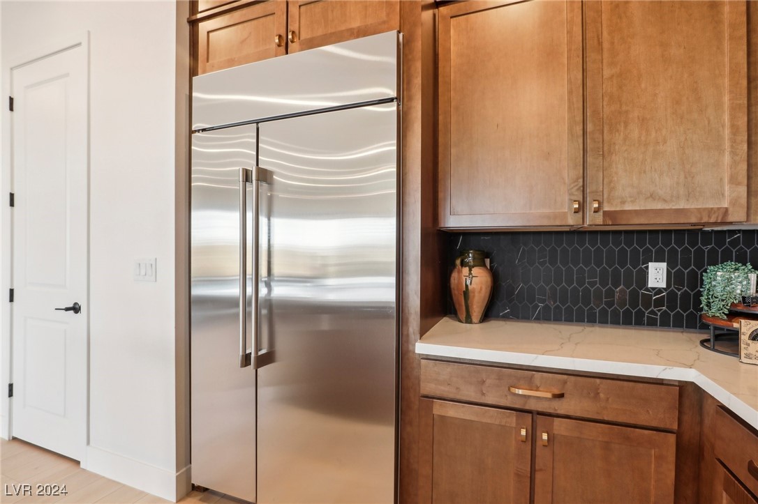Kitchen with wood cabinets, stainless steel refrigerator, pale counters, and dark geometric tile backsplash.