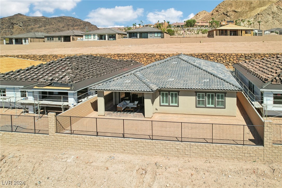 Aerial view of a beige single-story home with a gray tile roof, fenced yard, and covered patio.