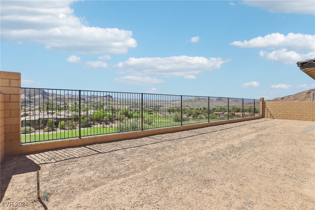 Gravel terrace with a black railing overlooking a green neighborhood and distant desert mountains.