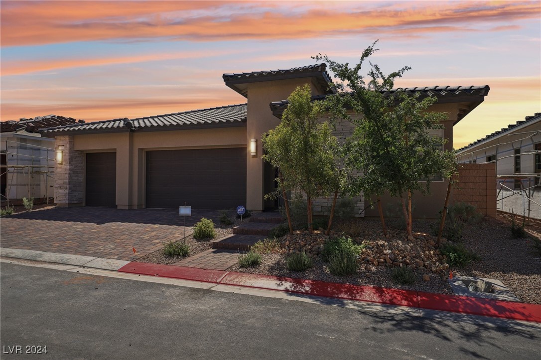 Modern stucco home with tile roof, three-car garage, and desert landscaping at sunset.