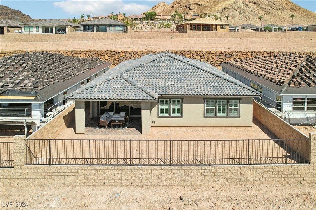Aerial rear view of a home with a covered patio, enclosed yard, and rocky mountain backdrop.