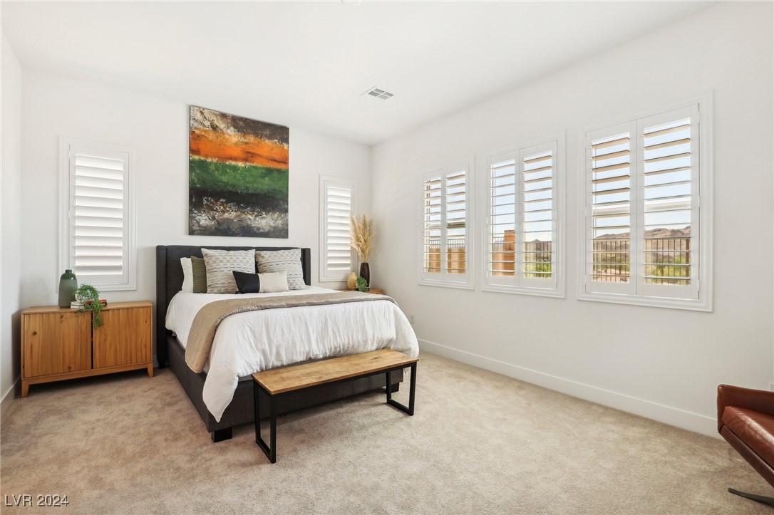 Staged bedroom with white bedding, plantation shutters, and desert hills visible through the windows.