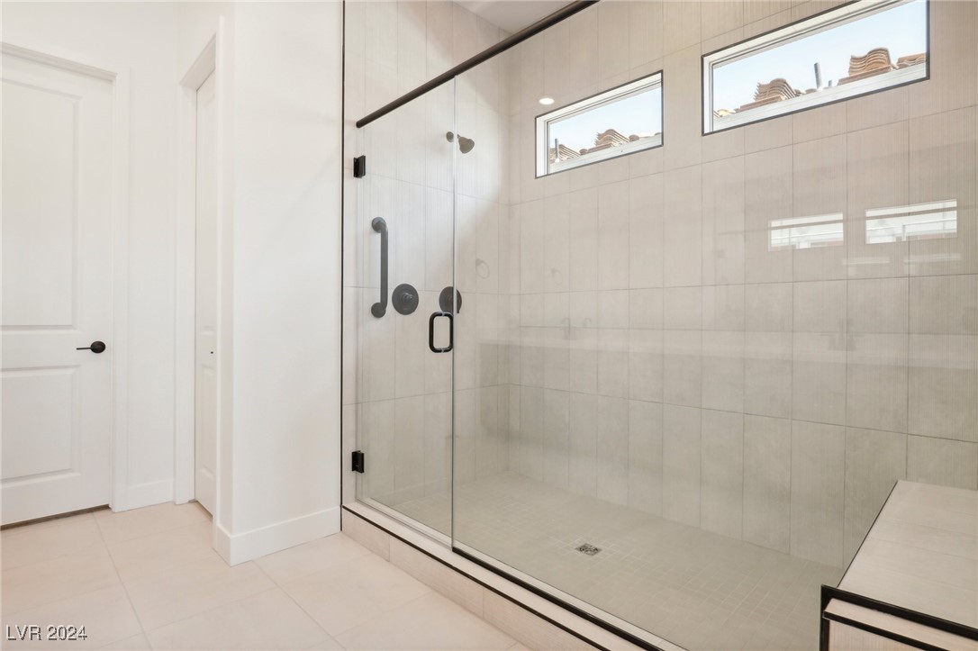 Walk-in shower with clear glass enclosure, pale tile, black fixtures, and two high windows.