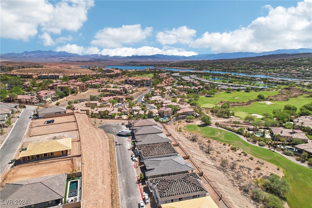 Aerial view of homes under construction beside a golf course, lake, and distant mountains.