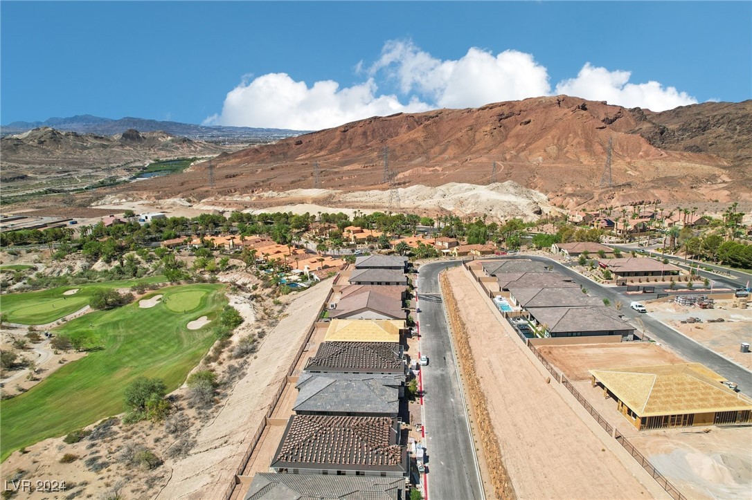 Aerial view of homes under construction beside a golf course, with desert mountains beyond.