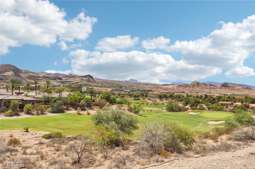 Golf course fairway and greens below desert mountains, viewed from a rocky hillside.