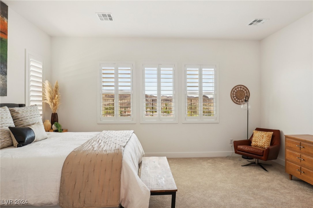 Furnished bedroom with shuttered windows overlooking distant mountains and a brown leather accent chair.