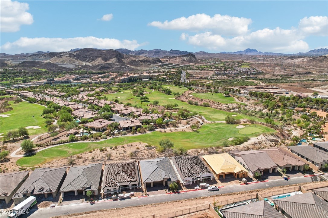 Aerial view of a home under construction beside a golf course, with desert mountains beyond.