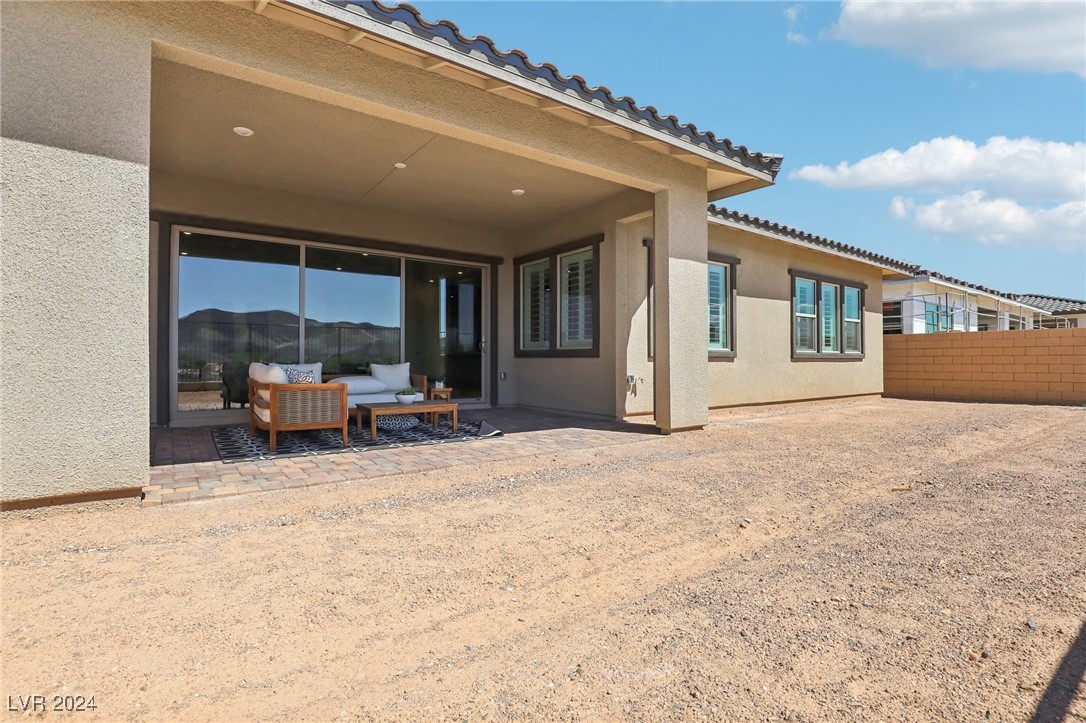 Rear exterior with covered patio, sliding glass doors, outdoor seating, and a gravel yard.
