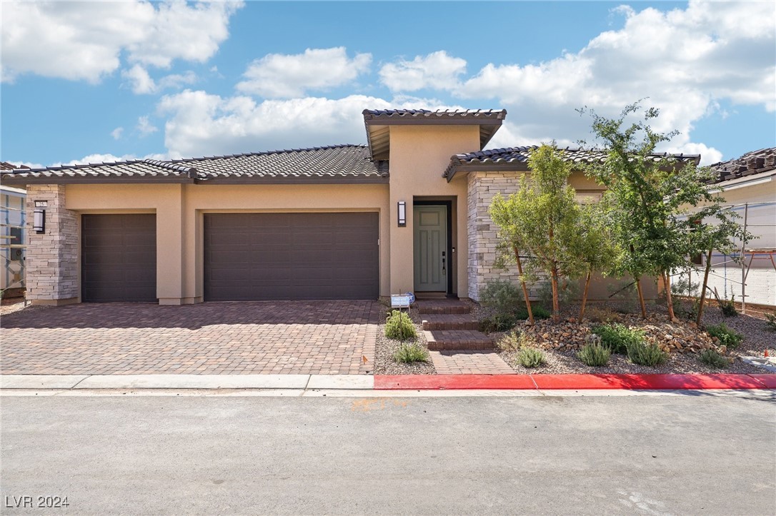 Single-story stucco home with stone accents, a paver driveway, and desert landscaping.