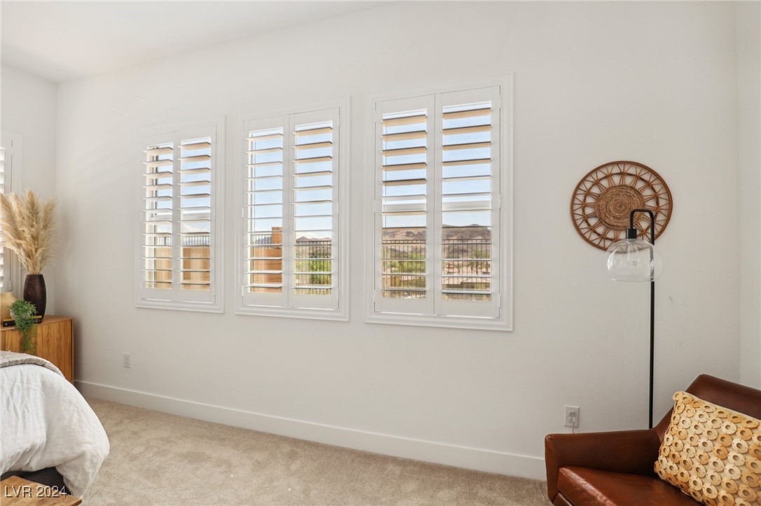 Bedroom with three shuttered windows, a white bed, and a brown leather chair.