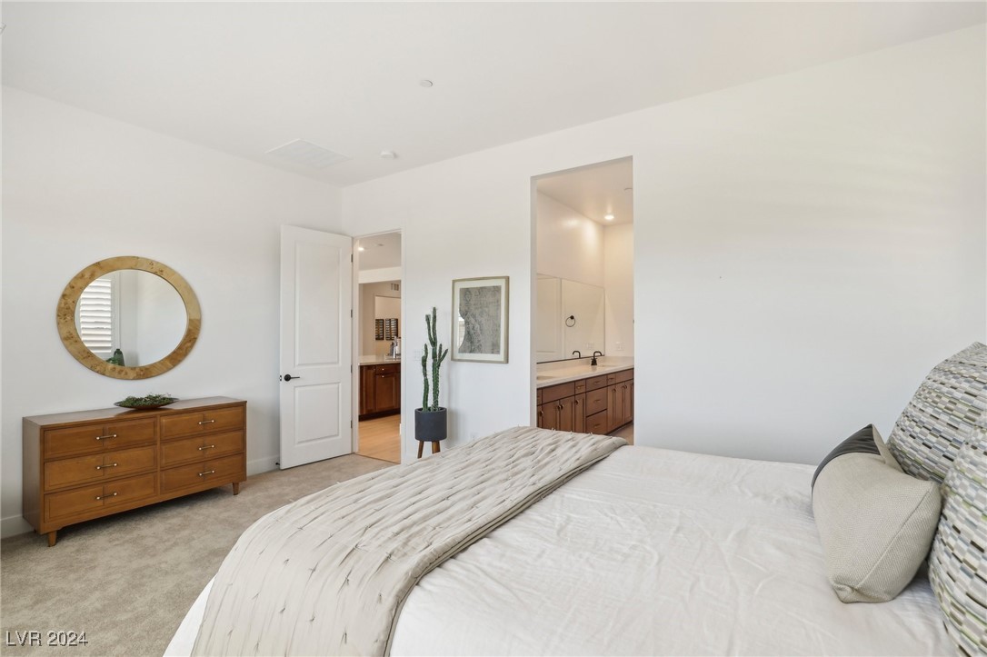 Furnished bedroom with a white bed, wooden dresser, round mirror, and open doorway to the bathroom.