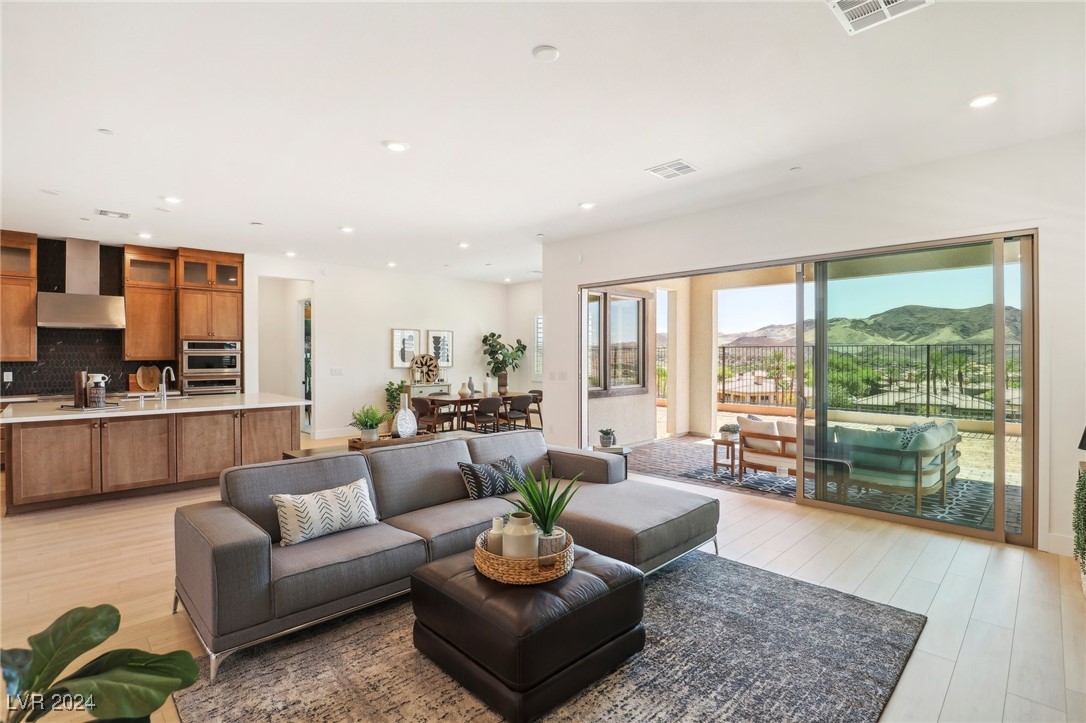 Open-plan living room with gray sectional, wood-cabinet kitchen, and sliding doors overlooking mountains.