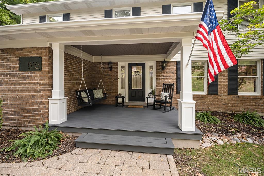 Brick home with a covered porch, hanging swing, rocking chairs, and an American flag.
