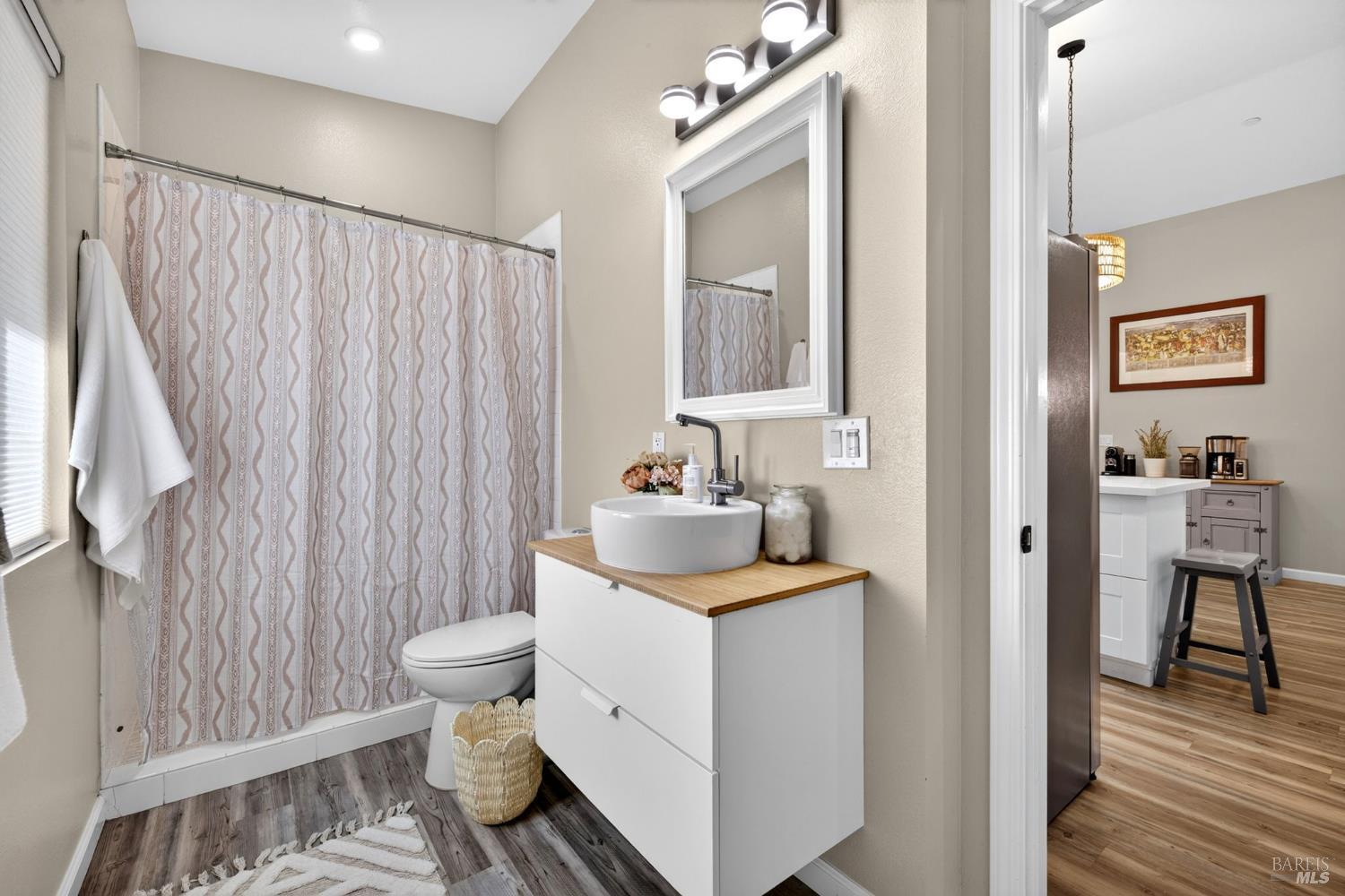 Bathroom with patterned shower curtain, wood-top vanity, and an adjoining room with a second vanity.